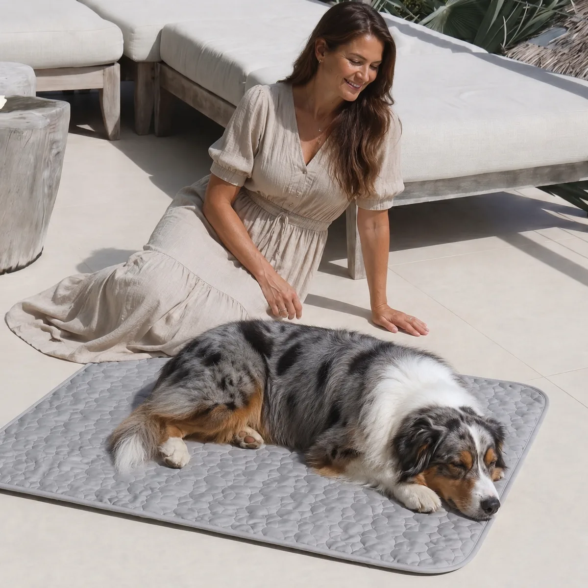 Femme accroupie sur une terrasse à côté d'un berger australien endormi sur un tapis rafraîchissant gris