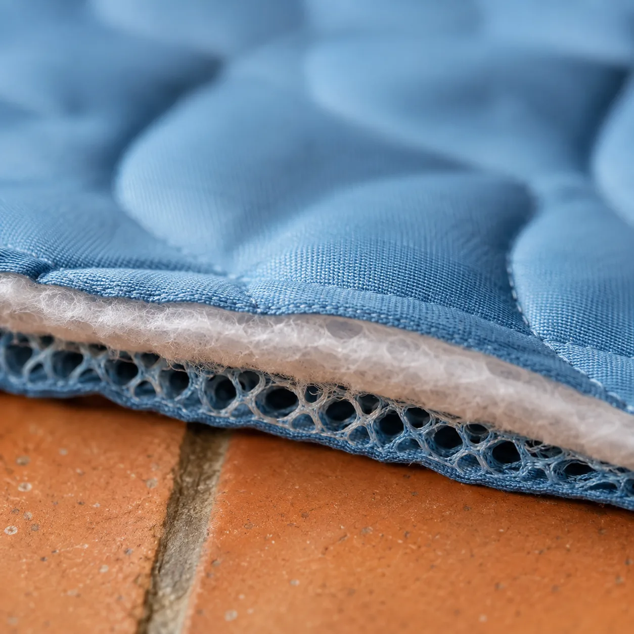 Vue rapprochée de la tranche du tapis Frimouf : dessus matelassé en soie glacée, ouate intermédiaire et maille aérée en dessous